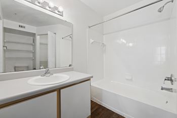 A white bathroom with a sink, mirror, and bathtub.